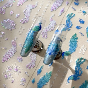 Sparkling peacock feather nail art stickers with glitter accents on long nail tips