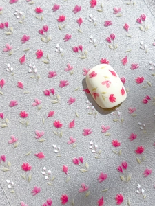 Dettaglio di adesivi per unghie con fiori rosa minimalisti su base bianco crema