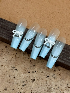 Detail of light blue gradient press-on nails with 3D white bows and wavy lace patterns