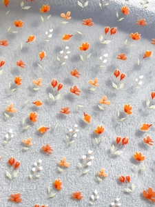 Dettaglio macro di adesivi per unghie con piccoli fiori arancioni e delicate foglie verdi