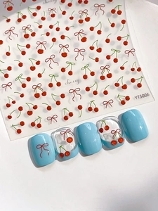 Dettaglio di adesivi per unghie con ciliegie rosse e fiocchi su manicure blu chiaro