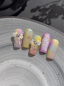 Macro shot of 3D bow and floral nail art stickers on pastel gradient press-on nails