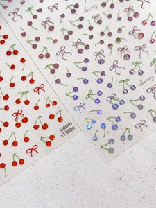 Vista macro di adesivi per unghie 3D con ciliegie, fiocchi ed effetto laser lucido