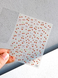 Dettaglio di adesivi traslucidi per unghie con motivi di ciliegie rosse e fiocchi