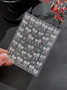 Detail of glitter laser ribbon and bow nail art stickers held against a black background