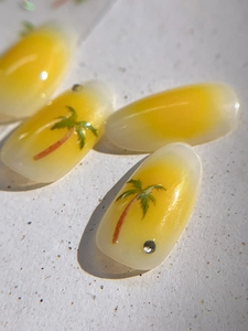 Macro shot of yellow gradient almond nails with green palm trees and small rhinestones