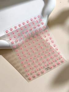 Detailed macro view of 3D embossed pink cat paw nail art stickers on a clear sheet