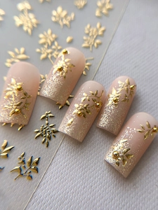 Makro-Detail von goldenen Blumen-Nailart-Anhängern und Folie auf rosa mattem Kunstnagel