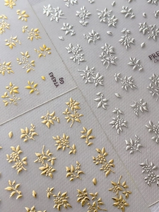 Makroaufnahme von 3D-Relief-Nagelaufklebern in Silber und Gold mit floraler Metallstruktur