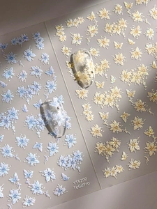 Detail of 3D embossed nail stickers featuring blue and beige floral and butterfly patterns