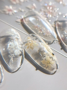 Macro shot of transparent nail stickers with embossed white floral patterns and tiny pearls