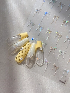 Détail d'autocollants pour ongles nœuds irisés avec perles sur manucure jaune