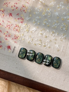 Detail of bamboo leaf nail art stickers with gold accents on dark green manicured nails