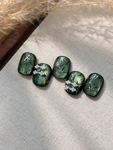 Macro detail of emerald green cat-eye press-on nails with bamboo motifs and pearls