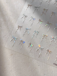 Détail d'autocollants pour ongles avec nœuds holographiques et reflets irisés brillants