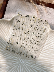 Detailed view of bamboo style nail stickers with green leaves on white ceramic plate