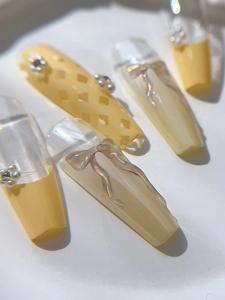Gros plan sur les ongles avec nœuds jaunes et transparents et strass floraux