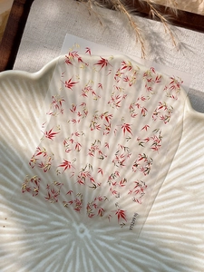Detailed view of autumn red maple leaf nail art stickers with golden accents on a ceramic tray