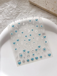 Détail de stickers à ongles cœur bleu et lune d'argent sur une assiette blanche