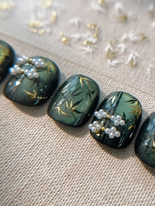 Detailed macro view of deep green cat-eye nails with golden bamboo leaves and pearls