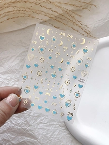 Vue détaillée des stickers ongles dorés avec motifs d'étoiles, lunes et cœurs bleus