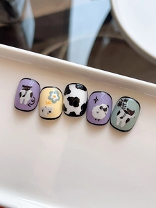 Détail de faux ongles peints à la main avec motifs mouton et vache sur plateau blanc