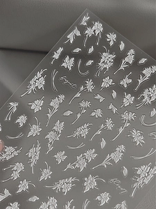 Nahaufnahme der weißen Blumen-Nagelsticker mit 3D-Prägung auf grauem Hintergrund