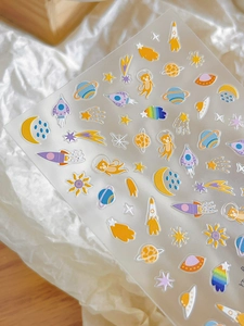 Detail of space-themed nail art stickers with rockets, planets, and cartoon cat