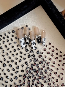 Détail macro de faux ongles léopard avec charms papillon en métal et pendentif cadenas