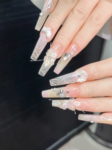 Macro detail of long coffin nails with 3D lily flowers, pearls, and aurora glitter