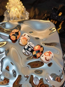 Macro shot of Halloween press-on nails featuring pumpkin, bat, and mummy designs on silver tray