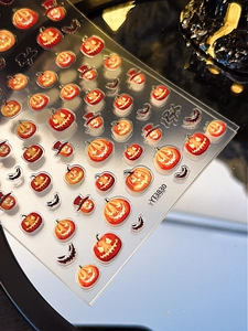 Close-up of Halloween pumpkin and bat nail art stickers with glossy orange finish