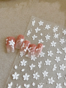 Macro shot of 5D white floral nail stickers and pearl accents on pink gradient press-on nails
