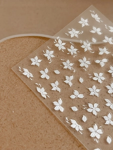 Macro detail of 3D embossed white floral nail art stickers with cherry blossom textures
