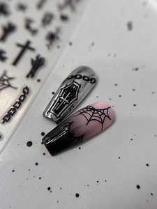 Macro shot of Halloween nail stickers with silver metal coffin and black spider web patterns
