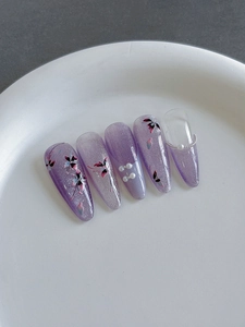 Détail de faux ongles dégradés violets avec motifs papillons et perles décoratives