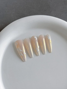 Détail d'ongles stiletto or champagne avec relief de fleurs 3D et éclat de perle