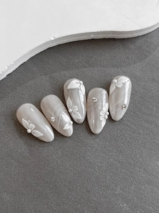 Detail of 3D embossed floral nail art with pearls and rhinestones on long oval nails