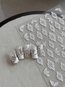 Detailed macro view of 3D embossed white floral nail stickers on a minimalist backdrop