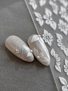 Macro detail of 3D embossed floral nail stickers with white petal patterns on pearl base
