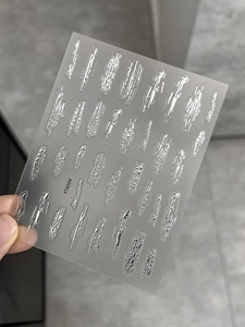 Makro-Detail von 3D-Präge-Nagelstickern in Silber mit Metalltextur und flüssigen Wellen