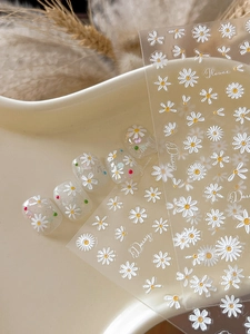 Detail of 3D embossed daisy nail stickers with floral patterns on transparent tips