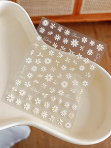 Macro detail of 3D embossed white daisy nail stickers with yellow centers on clear sheet
