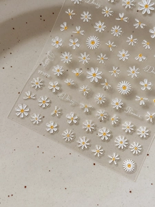 Detail view of 3D embossed white daisy nail stickers on a minimalist ceramic plate