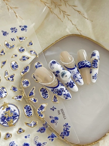 Blue porcelain nail stickers with gold accents and floral patterns on white nails
