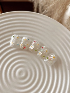 Detailed close-up of daisy nail stickers with colorful polka dots and glitter on ceramic tray