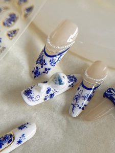 Macro shot of blue and white porcelain nail art with pearl chains and floral patterns
