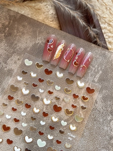 Detailed 3D heart nail stickers with gold edges shown on brown gradient nails