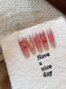 Detail of pink gradient press-on nails with metal hearts and rhinestones on soft texture