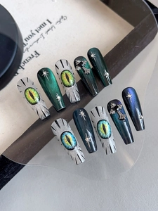 Macro detail of gothic press-on nails featuring 3D dragon eyes and metallic cross charms
